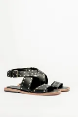 Sandalias bajas de cuero negro con tachas plateadas, tiras cruzadas y hebilla al tobillo.