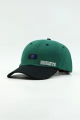 Gorra con visera de diseño bicolor, con cuerpo en color verde y visera en color negro. Presenta un parche rectangular con un punto azul en el centro y la palabra 'ENFANTS' bordada en blanco en el panel frontal.
