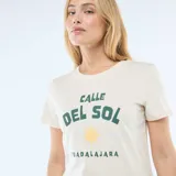 Remera de algodón color crema con cuello redondo y mangas cortas. Presenta un estampado frontal con el texto 'Calle del Sol' en color verde, un dibujo de un sol amarillo y la palabra 'Guadalajara' debajo.