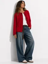 Cardigan de lana merino color rojo, con cuello redondo, mangas largas y cierre frontal de botones dorados. Presenta detalles de volados a lo largo de la botonera y bolsillos frontales simulados con solapa y botón.