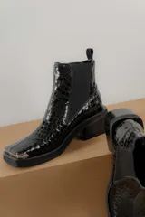 Bota corta tipo chelsea de cuero con textura croco, punta cuadrada con detalle metálico y suela de goma con taco bajo.