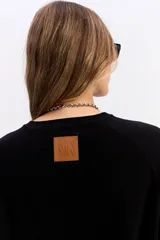 Sweater de punto negro con cuello redondo, manga larga y calce relajado. Presenta una costura vertical central en el frente y puños acanalados.