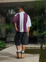 Chomba de piqué con diseño color block vertical en negro y verde oscuro, cuello polo y cierre frontal parcial. Presenta inscripciones en el frente.