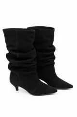 Botas de caña media con diseño slouchy color negro, confeccionadas en material sintético, con punta fina y taco bajo de aguja. Presentan efecto fruncido en la caña.