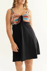 Malla entera con short y vestido negro, con corpiño estampado con motivos geométricos en tonos naranja, celeste y marrón. Presenta un nudo en el centro del escote para regular la profundidad.