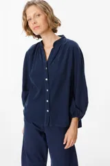 Camisa de pana azul marino con cuello mao, cierre frontal de botones y mangas largas abullonadas con puños elásticos.