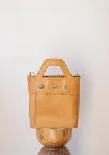 Bolso tipo tote de cuero color tostado con asa corta y correa larga desmontable. Decorado con tres piedras verdes.