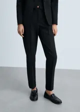 Pantalón de traje negro de tiro medio, con diseño recto y trabillas para cinturón. Cuenta con bolsillos laterales y dos bolsillos de ribete en la parte posterior, además de dobladillo vuelto en los tobillos.
