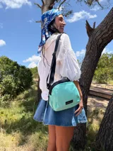 Bandolera de diseño compacto y moderno, confeccionada en tafeta liviana color verde agua. Cuenta con cierre superior, correa ajustable ancha de color negro y etiqueta frontal con logo de la marca.