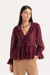 Blusa de tejido liviano color blanco, con escote en V y volados frontales. Presenta mangas largas amplias con puños fruncidos y un volado en el ruedo que le otorga un calce fluido y cómodo.