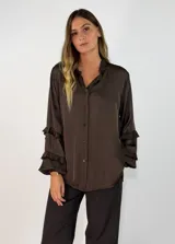 Camisa de satén color negro con cuello mao y volados en las mangas. Presenta cierre frontal con botones y diseño de corte holgado con largo asimétrico.