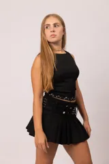 Pollera mini tableada de color negro, con diseño de tiro medio. Presenta un cinturón ancho integrado con apliques de tachas plateadas y cierre de doble botón metálico.