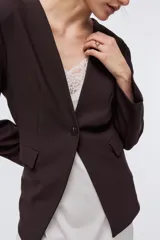 Blazer de punto marrón oscuro, de corte entallado con hombreras, escote en V sin cuello, cierre de un solo botón y bolsillos frontales con solapa.