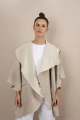 Ruana color crudo de lana fina sin teñir, con capucha, bolsillos y terminaciones envivadas. Tiene un broche para usar cerrada. Es una prenda oversize sin forro, cómoda, versátil y fácil de combinar.
