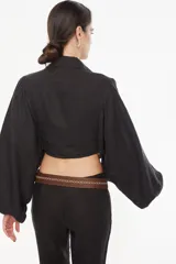 Top corto de lino italiano con diseño a cuadros en tonos verde oliva, beige y rosado, cuello camisero, mangas largas abullonadas con puños elásticos y nudo frontal ajustable.
