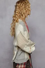 Cardigan de punto con diseño patchwork en bloques de color gris, blanco y beige, de manga larga abullonada, cuello en V y cierre frontal con botones.