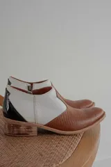 Botinetas de cuero con diseño bicolor, combinando cuero texturizado marrón en la puntera y cuero blanco granulado en los laterales. Presenta un detalle de charol negro en el talón y taco bajo de madera.