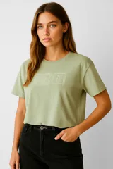 Remera de algodón color verde oliva, de corte holgado y cuello redondo a la base. Presenta un diseño bordado en el centro del pecho que simula dos estampillas postales.