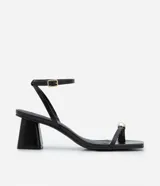 Sandalias negras de tacón ancho, con tiras finas, puntera cuadrada, adorno metálico dorado en el dedo gordo, cierre con hebilla en el tobillo y tacón mediano.