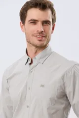 Camisa celeste de manga larga confeccionada en algodón, con cuello camisero, cierre frontal de botones, bolsillo en el pecho y diseño de cuadros sutiles.