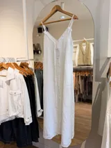 Vestido maxi de lino color blanco, con escote en V, tirantes finos regulables y detalles de flecos en el frente.