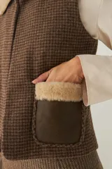 Chaleco corto de corte recto, confeccionado en lana fina sin teñir, con cuello de piel sintética y bolsillos frontales con detalles en cuero.