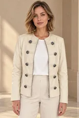 Campera de cuero ovino color beige, estilo napoleón, con cuello redondo, cierre frontal y botones metálicos decorativos en formato militar.