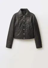 Chaqueta de cuero ovino en color negro con acabado en napa. Presenta cuello camisero, cierre frontal con botones a presión metálicos, bolsillos laterales y puños abotonados.