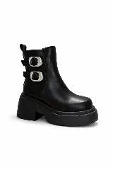 Bota corta de cuero sintético color negro, con plataforma gruesa y taco cuadrado. Presenta dos correas laterales con hebillas metálicas plateadas y puntera cuadrada.
