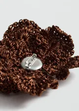Broche en forma de flor de gran tamaño, confeccionado en tejido de crochet color marrón, con detalle central de pistilos en hilo blanco y naranja.