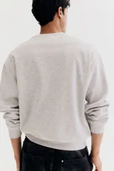 Buzo gris claro de corte holgado, con cuello redondo y mangas largas.