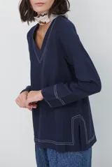 Blusa azul marino de corte recto y holgado, con escote en V y mangas largas. Presenta detalles de costuras a la vista en color blanco en el escote, puños y ruedo.