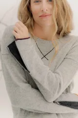 Buzo de lambswool color beige, con escote redondo y detalle en V. Presenta cierres metálicos en los puños que revelan un interior en contraste de color marrón y ribete rojo. Tiene tajos laterales para mayor comodidad y un fit amplio.