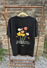 Remera negra con efecto acid wash, corte holgado y estampa trasera de flores con la frase 'Más Flores Menos Drama'.
