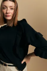 Sweater negro de manga larga, tejido suave y caída liviana, con volados en el delantero y mangas. Silueta recta.