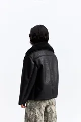 Campera de estilo aviador en color marrón oscuro, con exterior efecto gamuza e interior de corderito sintético color beige. Presenta cuello amplio, cierre frontal con botones y bolsillos laterales.