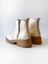 Bota corta de cuero vacuno con textura granulada, color crudo. Presenta cierre lateral metálico, suela track de goma en tono suela y tirador trasero.