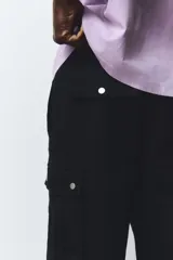 Pantalón cargo negro de corte holgado, con cintura elástica, bolsillos laterales, bolsillos tipo cargo con solapa y botón a presión en los laterales y bolsillos traseros con solapa y botón a presión.