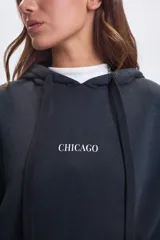 Canguro oversize de color negro con capucha y bolsillo frontal. Presenta una estampa gráfica en la espalda con la palabra Chicago y texto descriptivo en tipografía combinada.