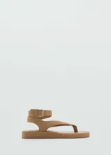 Sandalias planas de tipo dedo o thong, color marrón tostado, confeccionadas en piel bovino con acabado de gamuza. Tienen diseño de tiras anchas, puntera redonda y tira al tobillo con hebilla metálica dorada.