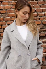 Tapado de paño color rosado, de corte oversized y diseño cruzado. Presenta solapas clásicas, mangas largas con puños vueltos y amplios bolsillos delanteros. Cierre frontal con un botón visible.