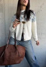 Cardigan de tejido de punto con diseño jacquard en la parte superior, cuello redondo y cierre frontal con botones. Presenta un patrón geométrico en tonos gris y azul sobre base color crema.