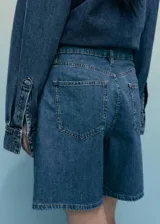Short de denim azul de tiro medio, con bolsillos laterales, bolsillos traseros, trabillas para cinturón y detalle de pinzas delanteras.