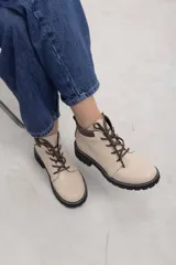 Borcego de cuero vacuno color marrón caramelo con acabado mate, estilo combate y caña baja. Cuenta con cordones marrones, panel de gamuza oscura en el cuello y suela de caucho negra tipo tractor con costura blanca visible.
