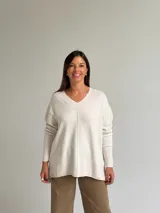Sweater de punto color beige con escote en V, diseño holgado y costura central vertical. Presenta mangas largas con puños acanalados y ruedo con terminación acanalada.