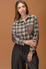 Camisa de manga larga con diseño a cuadros en tonos grises, marrones y ocres. Presenta cuello clásico, cierre frontal con botones, un bolsillo frontal y parches en los codos en contraste de color marrón.