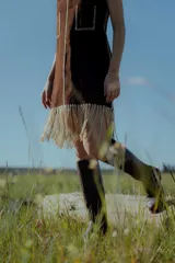 Vestido corto negro sin mangas, con escote en V y detalle de flecos en el ruedo. Presenta bordados en color blanco en el escote, los bolsillos y el centro del vestido.