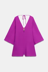 Mono corto de color fucsia, con escote en pico delantero y en la espalda, mangas anchas y largas, y detalle de fornitura dorada en el escote delantero con tiras finas para atar en la espalda.