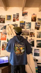 Hoodie azul de corte holgado con capucha y bolsillo frontal tipo canguro. Presenta un bordado circular en la espalda con un paisaje natural, una van y la frase 'Let's Explore Together'.