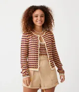 Chaqueta de punto de manga larga, cuello redondo y cierre frontal con botones de madera. Presenta un patrón de rayas horizontales en zigzag con colores crema, mostaza, fucsia y morado.